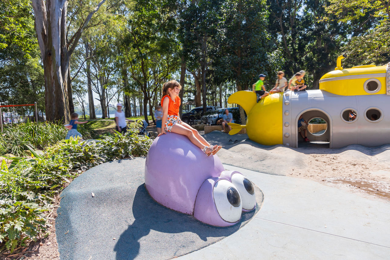Young girl atop a play structure in Colmslie Beach Reserve playground at Murarrie. Other children and adults in background.