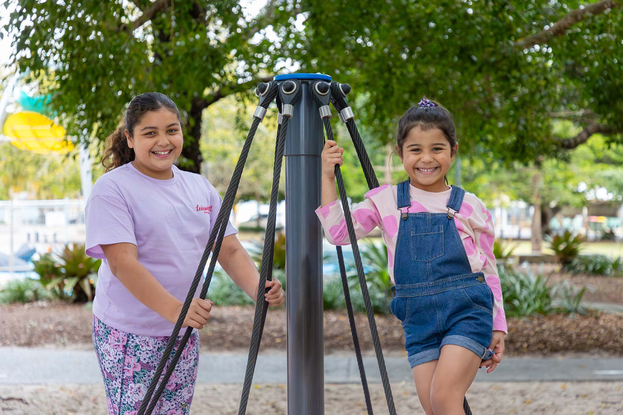 Two girls on a modern roundabout in Wynnum Wading Pool Park playground.