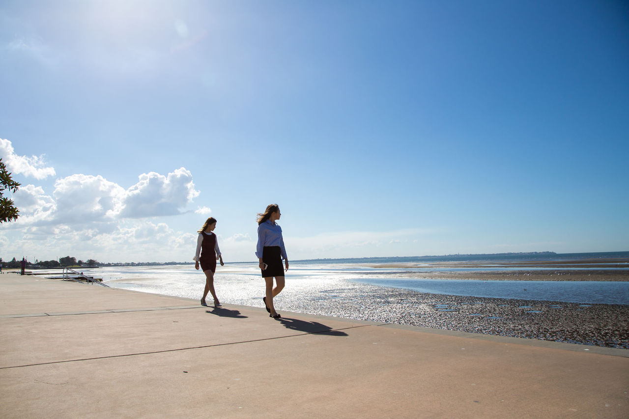 Two females walking along Sandgate foreshore on a sunny day, looking towards the water.