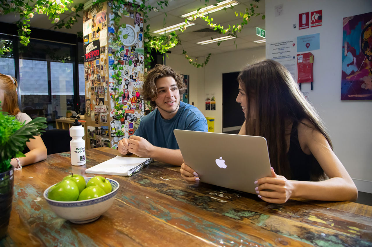 Two young people sitting at a table working on a laptop.