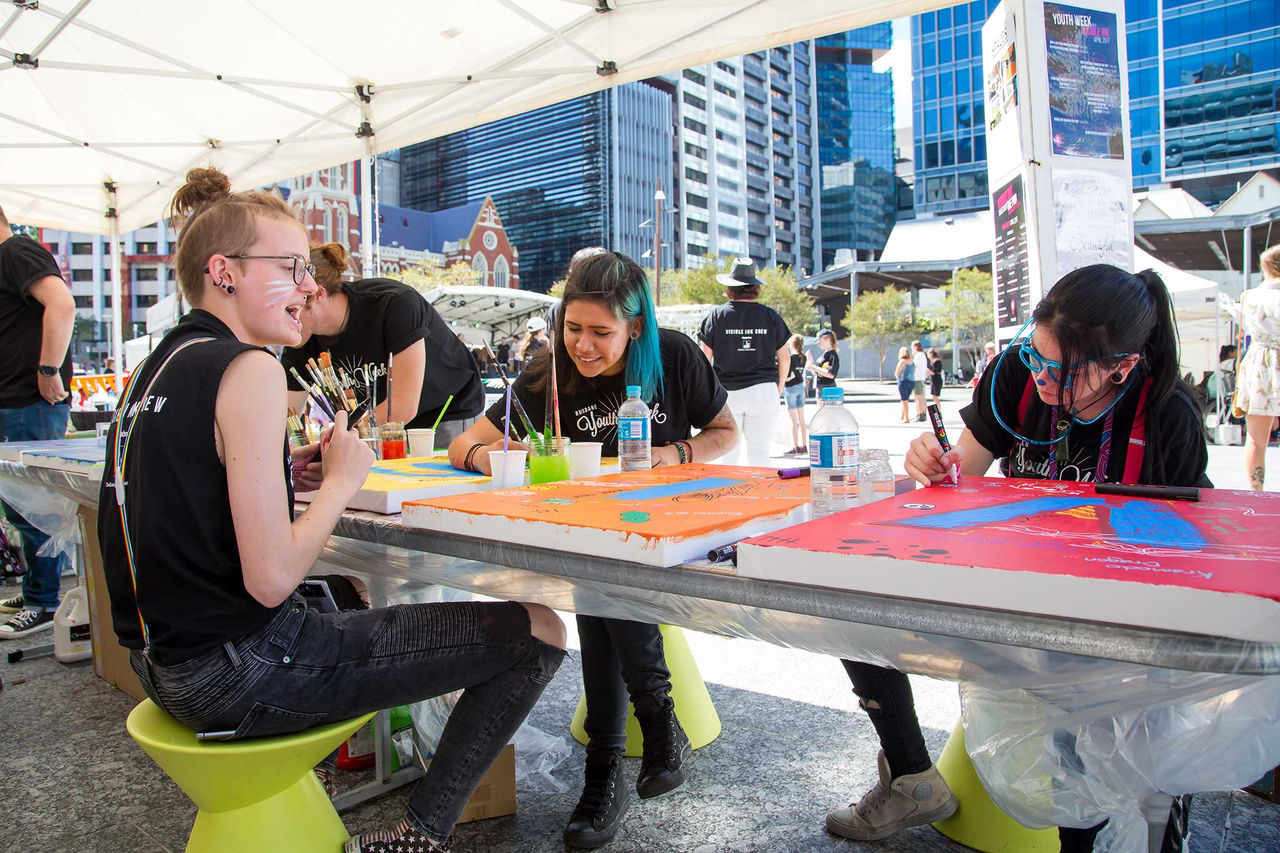 Young people sitting at a table in King George Square painting artwork.