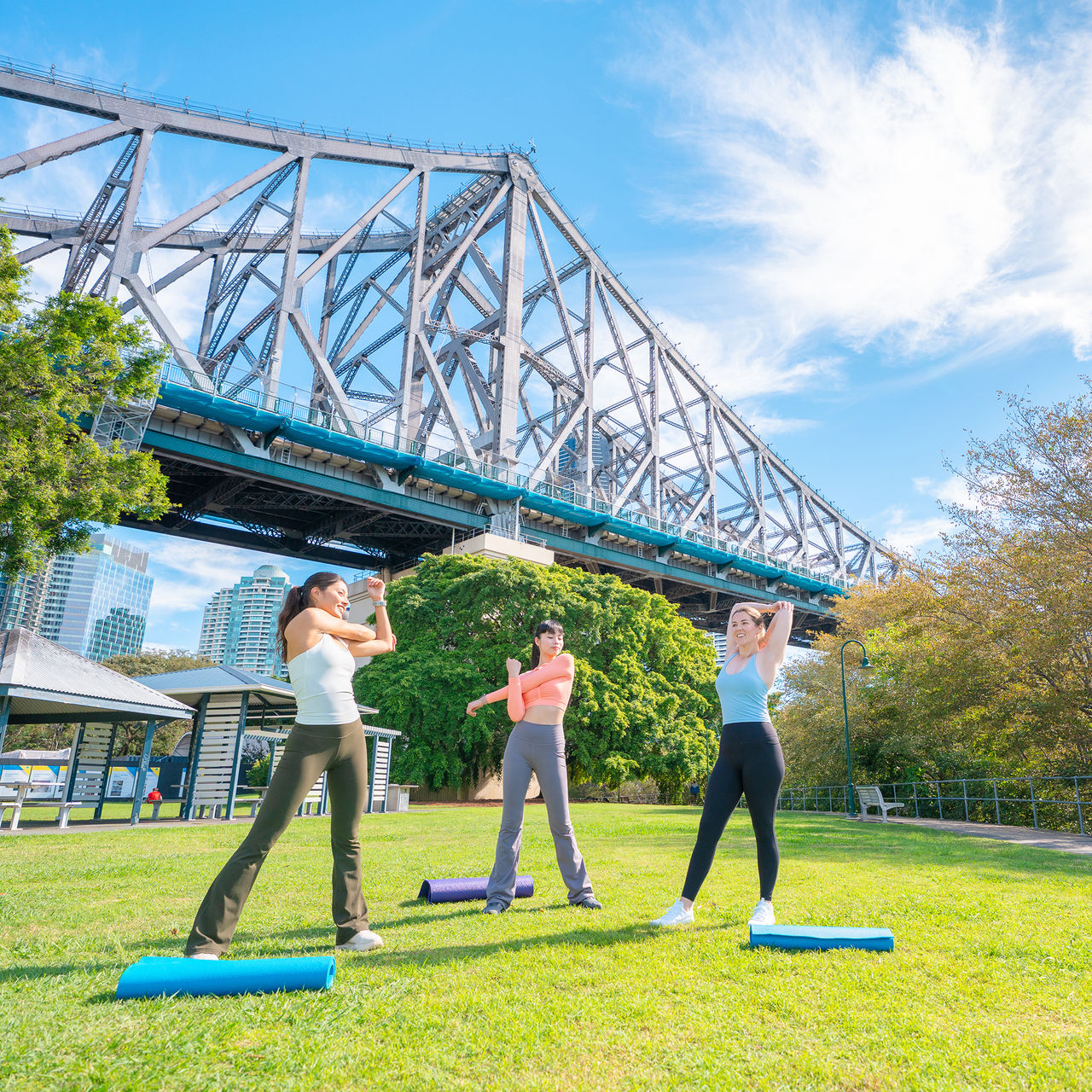 Three women warming up for a work out in a park near the Story Bridge.