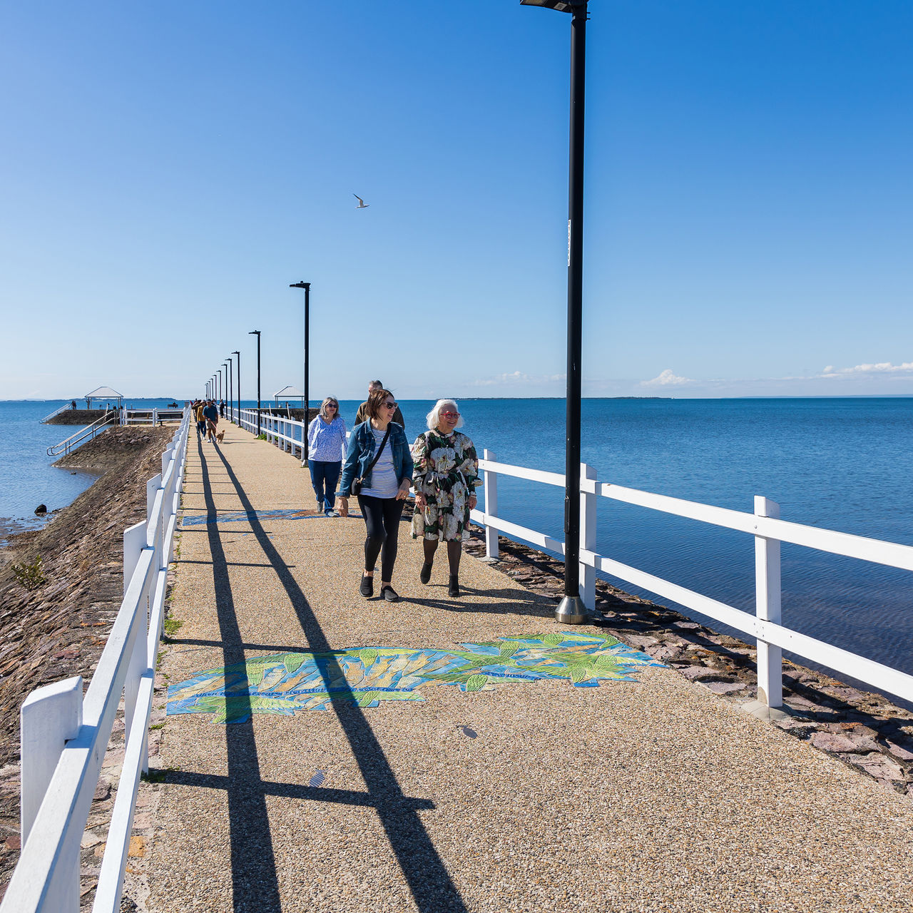 An elder woman, a younger woman and a couple walking on a pier