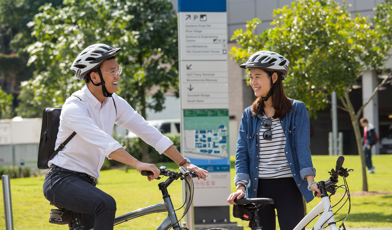 Two university students smiling at each other, one on the bike and the other standing next to the bike.