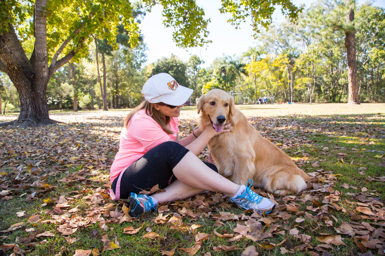Woman in activewear sitting cross-legged on ground in a Brisbane dog park, with a yellow Labrador by her side.