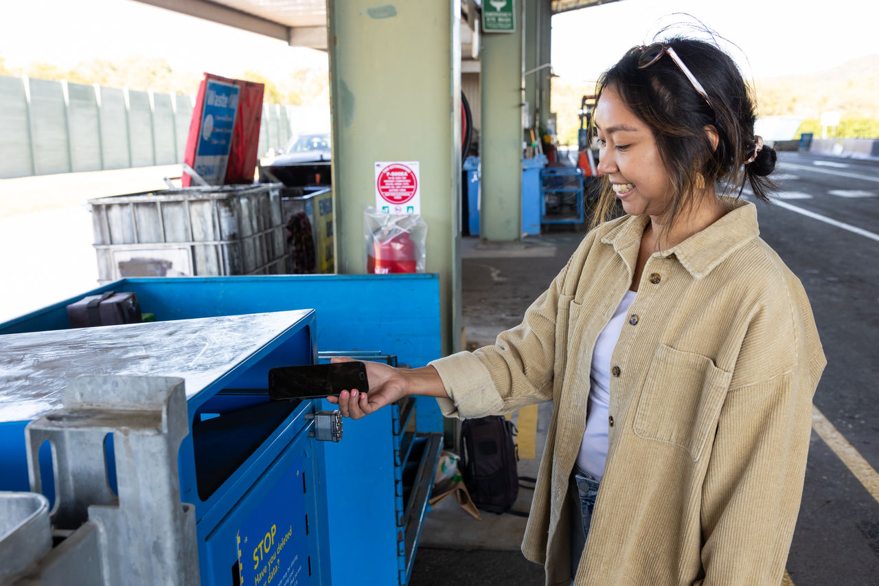 Female placing a smartphone in a phone recycling bin at a Council resource recovery centre.