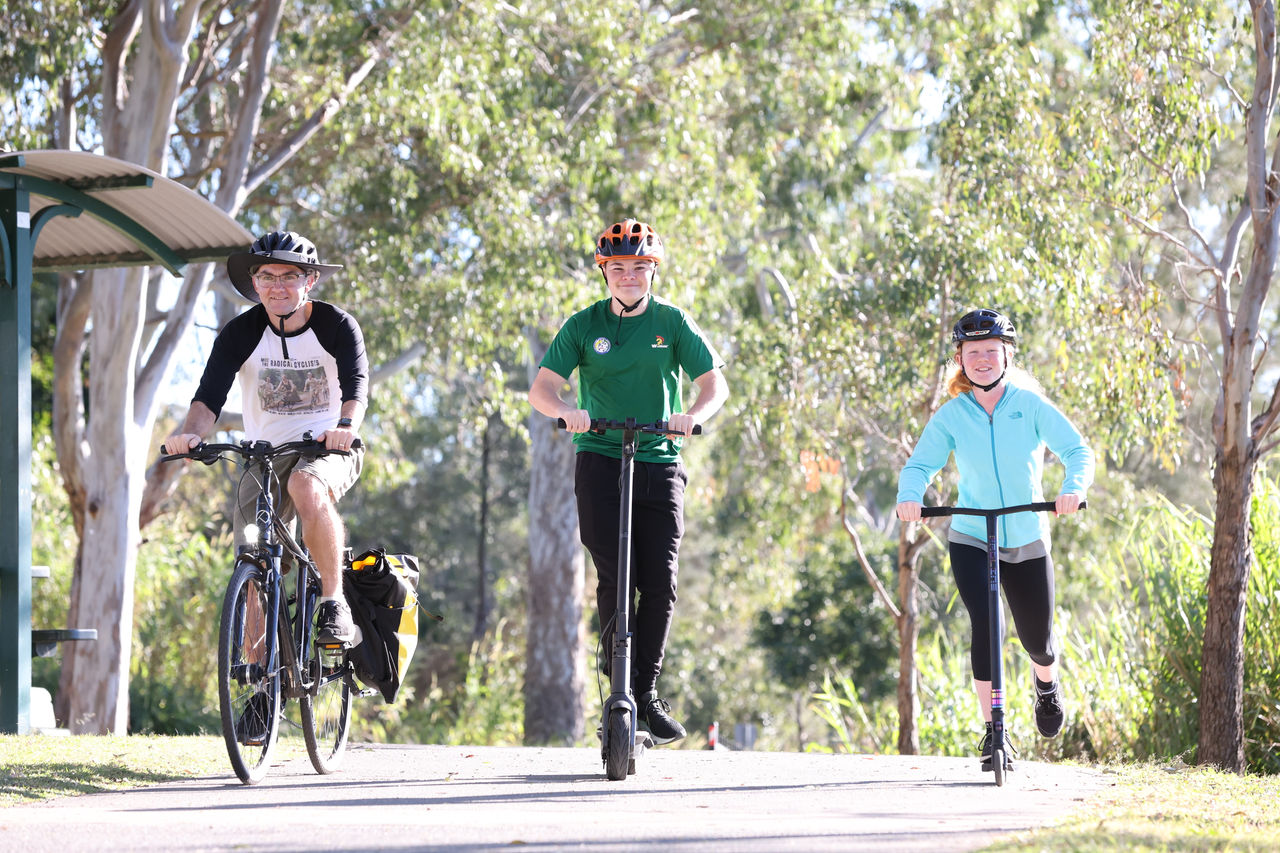 A male cyclist and a male and female on scooters on a path at Rocks Riverside Park.