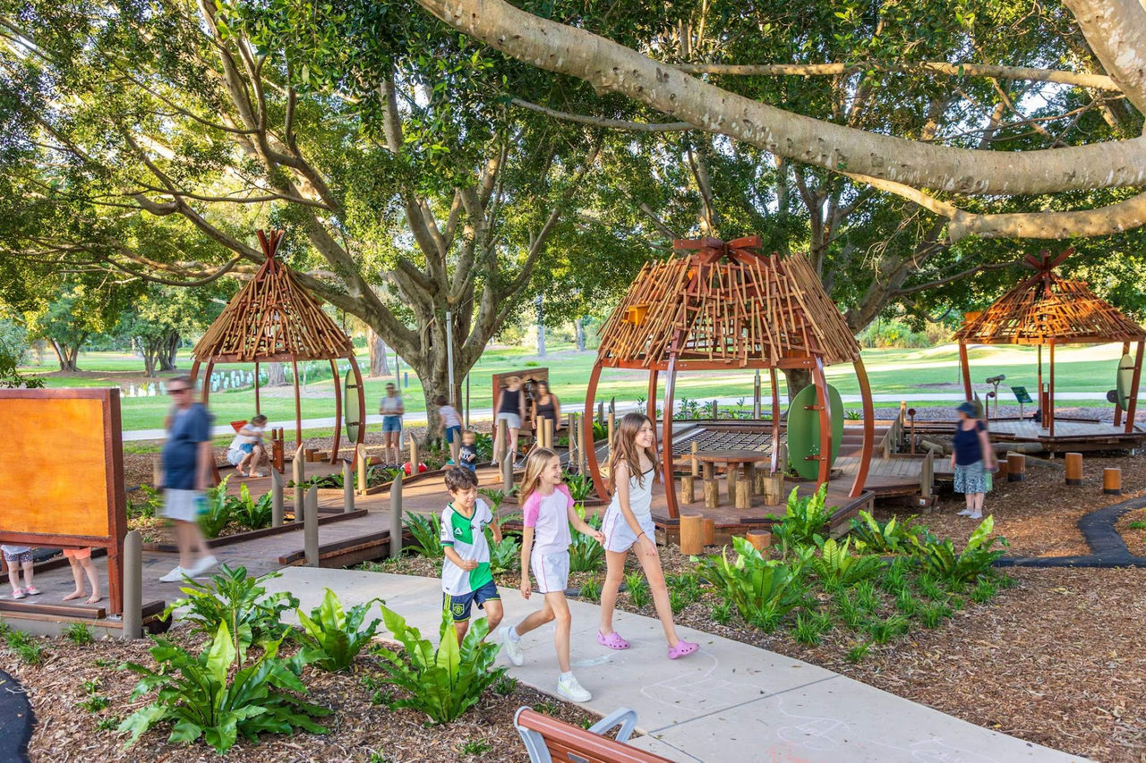 Children playing on a nature-themed playground, featuring trees and greenery. 