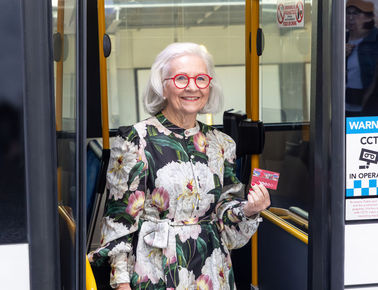 Female, senior bus passenger alighting from rear door on a Council bus with her senior go card in hand.